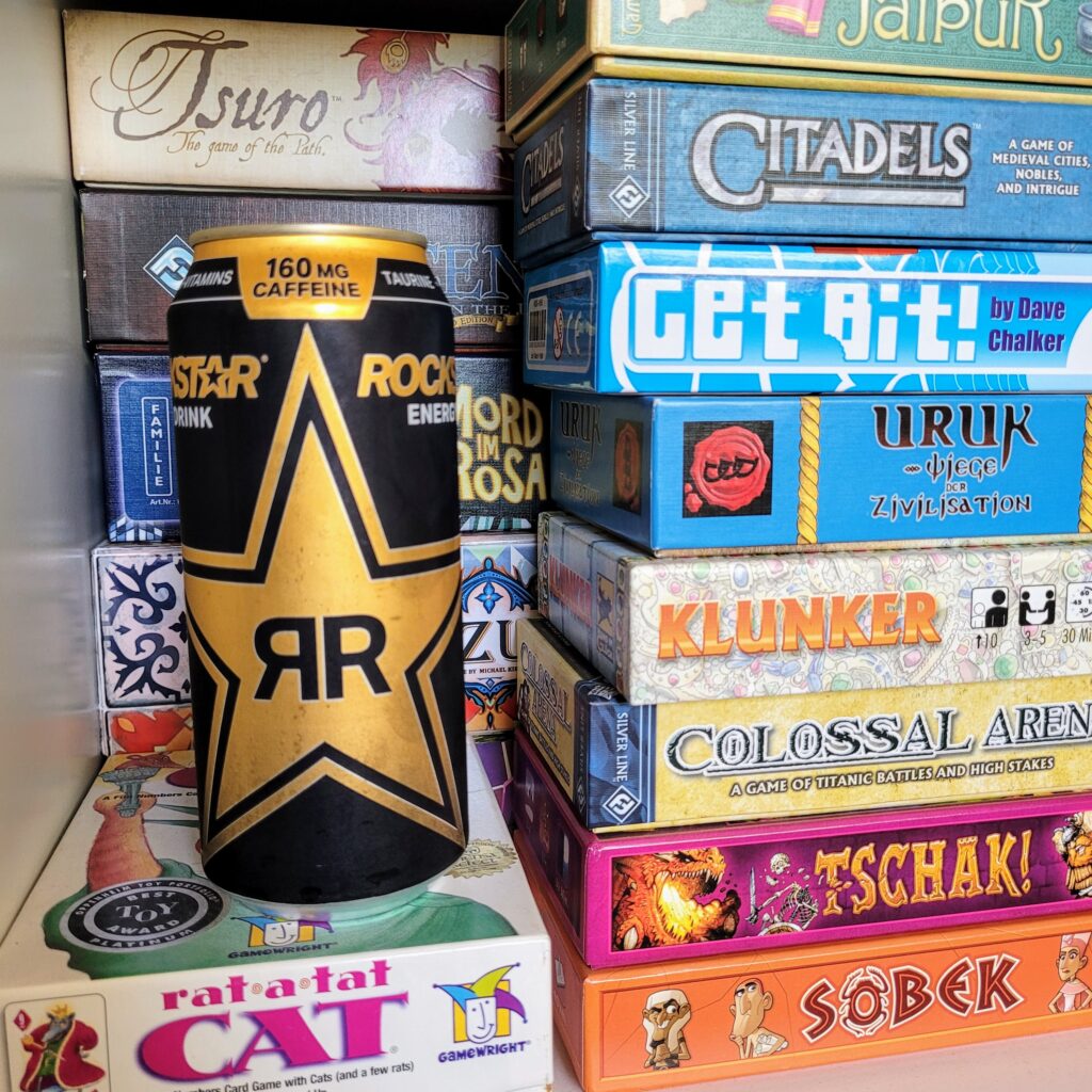 A Rockstar energy drink sits on a shelf with a lot of board games.
